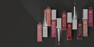 Stack of Pure Cosmetics lip gloss tubes in various shades on dark background