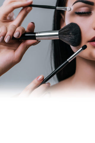 Person applying makeup with brushes to a woman's face.