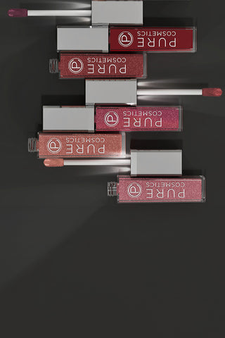 Stack of Pure Cosmetics lip gloss tubes in various shades on dark background