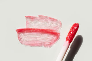 Pink lip gloss with application strokes on a light gray background