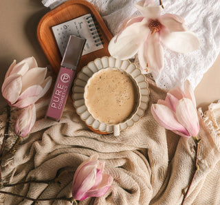 Pure Cosmetics On Pointe clean lip gloss styled with coffee, flowers, and cozy textures for a soft fall beauty flat lay.