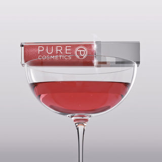 Pure Cosmetics Wineberry Light Up Lip Gloss resting on a wine glass, showcasing the rich berry hue of the fall shade of the month.