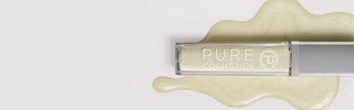 Pure Cosmetics Gloss of the Month in Clear. Sleek silver-capped butter-yellow gloss with shimmering swatch background, high-shine clean beauty.